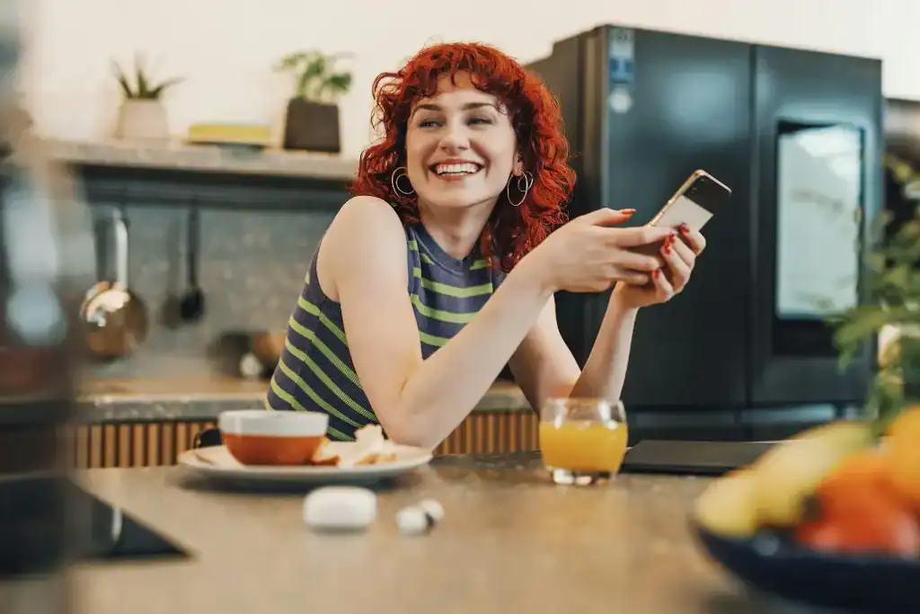 Woman with red hair sitting at a kitchen table drinking orange juice and being on her phone | local seo