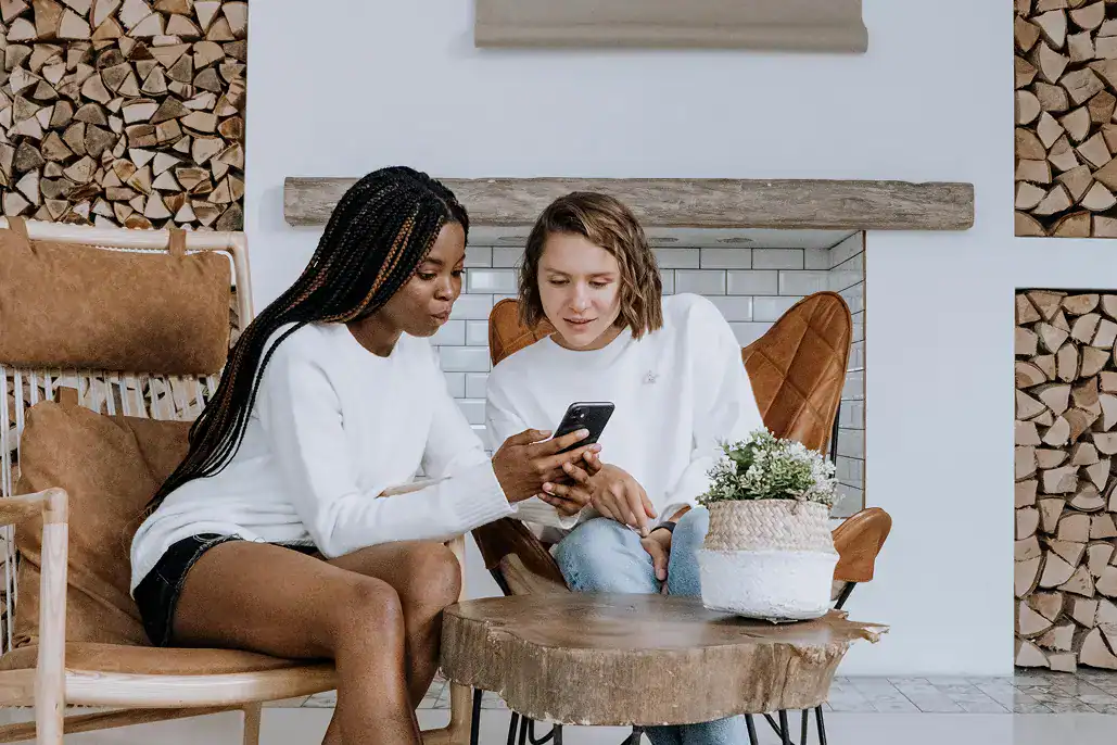 Two woman sitting on chairs showing each other something on a phone